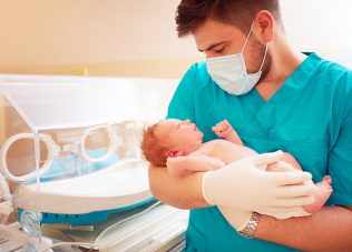 young adult man holding a newborn baby in hospital